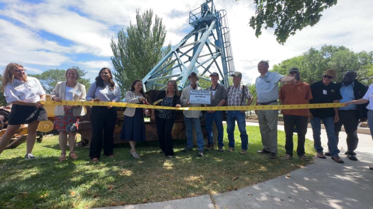 State officials, contractors and New Mexico Mining Museum representatives cut a ribbon June 18 to celebrate the donation of a historic uranium mining loader to the museum. Roger Siegmann, center, holds a sign describing the vintage uranium mining dump truck and winch, which will now be part of the museum’s public display. Diego Lopez - CCs
