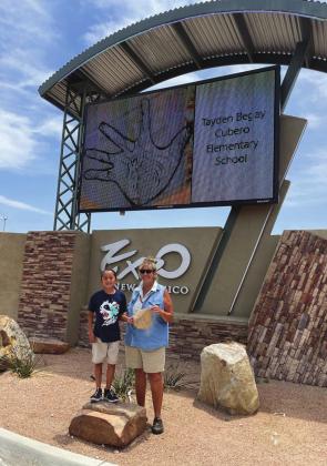 Second grader Tayden Begay and his art teacher, Debra Woodward, stand in front of Begay’s artwork which is being featured on an electronic billboard at the State Fair Grounds in Albuquerque, New Mexico. Courtesy photo