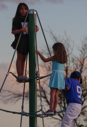 Children climb a playground rope structure beyond the outfield fence during a Little League game in Grants, N.M., on Thursday, July 9, 2026. While the action unfolds on the field, siblings and friends enjoy the evening at the park. PHOTOS by Jay Langford, AJJ Student Jounralist