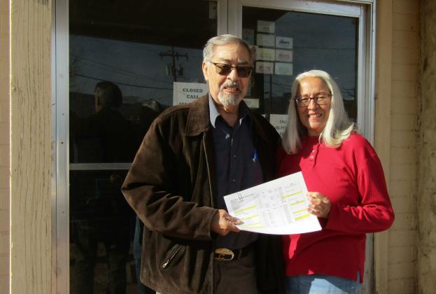 Evelyn Siegmann hands Grants-Milan Rotary Club Treasurer Nestor Griego a check for $3,103, raised from local businesses and sponsors. The funds support the beloved annual tradition started by Evelyn and her late husband, Roger Siegmann, where local children spread holiday cheer by painting festive Christmas designs on business windows throughout the community. Photos by Roger Siegmann